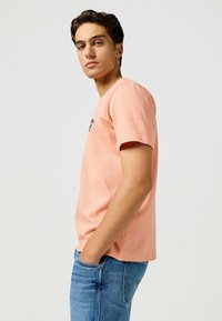 Paita puuvillasta, persikanvärinen, lyhythihainen ja pyöreällä kaula-aukolla. Rintakehässä pieni painettu kuvasto. Yhdistetty sinisiin farkkuihin.