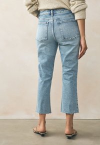 Světlé modré, nakrátko střižené rifle s vysokým pasem, s třepeným lemem a zadními kapsami. Nošené s plochými sandály s pásky a hadím vzorem.