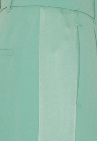 Myntgröna byxor med en slät textur, med en kontrasterande satinsnod och sidfickor. Skräddarsydd passform med en elegant design.