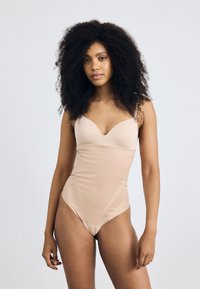 Naaktkleurige bodysuit met een diepe halslijn, gladde textuur en dunne verstelbare bandjes. Beschikt over naadloze zijkanten en een minimale bedekking.