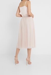 Ljusrosa klänning med satintopp och tyllkjol som har vita prickar, tillsammans med nakna högklackade sandaler.