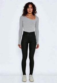 Sivý bodysuit s dlhým rukávom a asymetrickým výstrihom, kombinovaný s čiernymi legínami s vysokým pásom a bielymi teniskami. Hladké textúry.