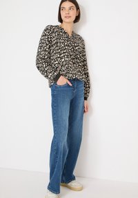 Sort og beige trykt bluse med lange ærmer, stylet med blå straight-leg jeans og beige sneakers med tekstureret sål.