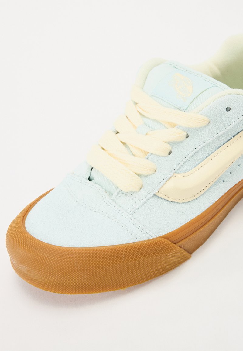Baskets en daim bleu clair avec une bande crème, des lacets crème et une semelle en gomme texturée. Présente un logo sur la languette et des détails cousus.