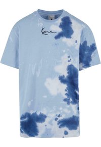 Světle modré bavlněné tričko s tie-dye vzorem v různých odstínech modré, s černě potištěným podpisovým logem v levém horním rohu.