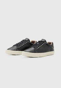 Schwarze Leder-Sneaker mit abgerundeter Zehenpartie, flacher weißer Gummisohle und kontrastierenden Schnürsenkeln. Dezentes Logo-Detail an der Seite.