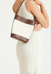 Taschen in Sand- und Cremetönen mit einem glatten Ledertragegurt und einem runden Verschluss. Strukturierter Stoffeinsatz als Kontrast zu den soliden Lederelementen.
