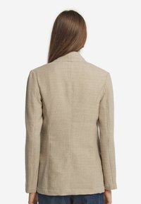 Beige strukturerad jacka med skräddarsydd passform, slagkrage och långa ärmar; har ett subtilt våffelmönster över hela ytan.