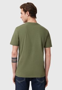 T-paita lyhyillä hihoilla, oliivinvihreä, pyöreällä kauluksella. Valmistettu pehmeästä kankaasta, jossa on suora helma ja minimaalinen ompelu yksityiskohtia.