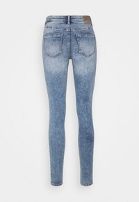 Jeans de denim azul claro y ajustados, con un acabado desgastado, cinco bolsillos y una etiqueta de cuero marrón en la cintura.