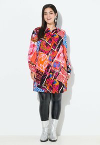 Kleurvolle, gestippelde jurk met lange mouwen, met geometrische en bloemige ontwerpen in rood, roze, blauw en zwart. Gecombineerd met zwarte leggings en zilveren laarzen.