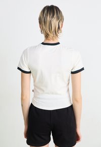 White short-sleeve t-shirt with black ribbed accents at the neckline and sleeves, fitted design, smooth fabric, and a visible tag on the side.