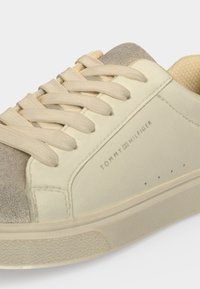 Κοντινό πλάνο ενός μπεζ και γκρι casual sneaker με μπεζ κορδόνια και το λογότυπο Tommy Hilfiger στο πλάι.