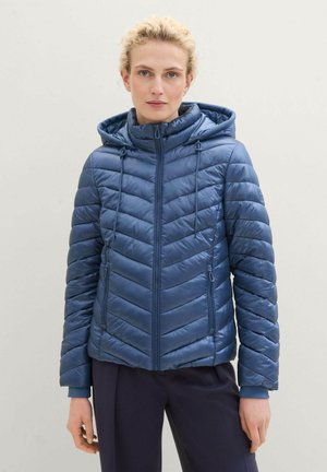 Gewatteerde blauwe jas met een capuchon, voorzien van een rits aan de voorkant, elastische manchetten en chevronstiksels voor textuur. Inclusief twee zijzakken.