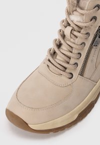 Beige ankelstøvle med glat læderoverdel, teksturerede snørebånd, sidelukning med lynlås og gummisål. Har blød foring og detaljeret syning.