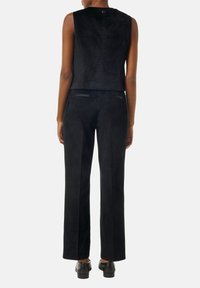 Schwarzes Wildleder, ärmelloses Oberteil, kombiniert mit passenden, taillierten Hosen; beide verfügen über eine glatte Textur und dezente Taschenakzente auf der Rückseite.