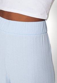 Närbild av midjan som bär ljusblå ribbade byxor med elastisk midja och en vit kort t-shirt.