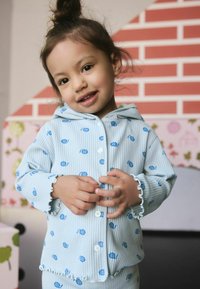 Light blue ribbed pajamas with a hood, featuring small blue floral prints and ruffled cuffs. Buttons down the front. Soft fabric texture.