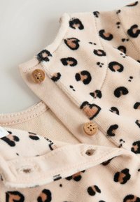 Tan fabric with black and brown leopard print; features wooden buttons and soft texture; designed with a collar and snap closure.