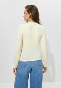 Lys gul langærmet top med et tætsiddende design. Struktureret stof og rund halsudskæring, kombineret med højtaljede blå jeans.