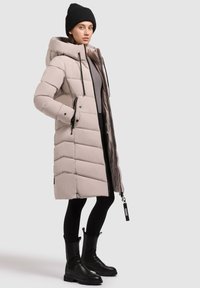 Gai bežs pūkains mētelis ar kapuci, ar horizontālu pildījumu un priekšējiem rāvējslēdzējiem. Melni akcenti un garas melnas zābaki noslēdz izskatu.