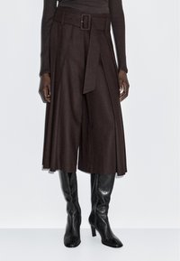 Culottes amples marron foncé avec une ceinture assortie, portés avec des bottes en cuir noires à talons hauts arriver au genou et un haut ajusté à manches longues.