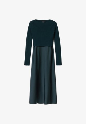 Donkergroene, langärmelig, cropped gebreide trui over een bijpassende lange satijnen rok, weergegeven tegen een witte achtergrond.