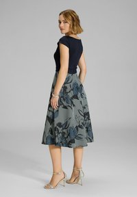 Top de marina ajustado con mangas tipo farol, falda fluida con estampado en azul y gris, con rayas verticales y acentos florales; sandalias plateadas de tacón.