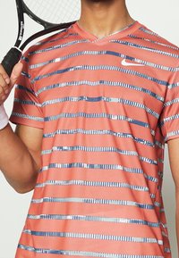 Camiseta de manga corta de color rojo-anaranjado con escote en V y rayas horizontales azules y plateadas. Textura suave, diseñada para ropa activa.