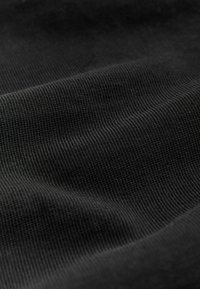 Schwarzer gerippter Stoff mit feinen vertikalen Linien und sanften Falten, die eine weiche Textur und Schatten erzeugen.