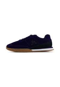 Sneaker low-top con tomaia in suede nero e viola scuro, suola texturizzata marrone e logo nero laterale, mostrato in profilo su sfondo bianco.