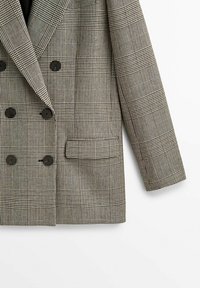 Veste à double boutonnage avec boutons noirs, motif à carreaux beige et noir, une poche avant et manche longue visible côté droit.