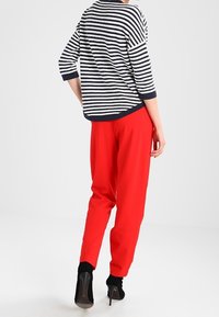 Gestreiftes navy- und weißes, lässiges Oberteil mit drei Viertelärmel, kombiniert mit hoch taillierten roten Hosen und schwarzen High Heels.