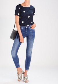 Blusa de lunares azul marino, combinada con jeans ajustados de un azul claro y tacones abiertos a rayas. Bolso negro de hombro con un diseño sencillo.