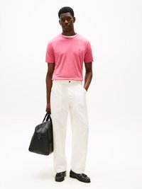 Ροζ βαμβακερή μπλούζα με στρογγυλή λαιμόκ�οψη, λευκά παντελόνια με φαρδιά γραμμή, μαύρη δερμάτινη τσάντα και loafer παπούτσια. Απλός σχεδιασμός, λεία υφή και αντιθετικά χρώματα.