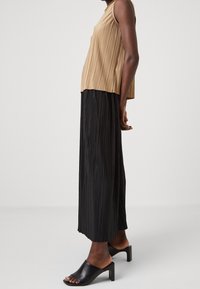 Top beige con pliegues combinado con una falda negra con pliegues. Mules negras de tacón completan el conjunto, mostrando un diseño simple y fluido.