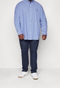 Jasnoniebieska i biała koszula w kratę na guziki, z długim rękawem, zestawiona z ciemnymi dżinsami i białymi tenisówkami. Posiada klasyczny kołnierzyk i guziki z przodu.