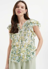 Bloemige blouse met knopen in het wit, groen en geel, met volants aan de mouwen en een lichte, wijde pasvorm. Gemaakt van lichtgewicht stof.