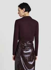 Haut bordeaux à manches longues avec un col montant, associé à une jupe crayon marron foncé brillante. Silhouette élégante et ajustée avec des détails soignés.