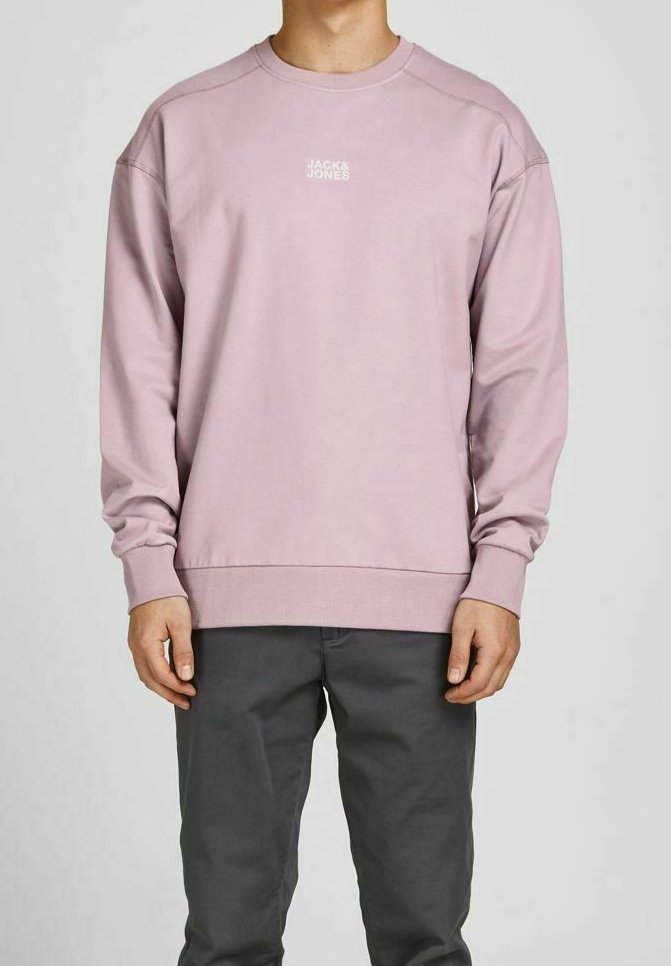 Ljusrosa sweatshirt med rund halsringning, långa ärmar och ribbad nederkant. Har en liten vit logotyp på bröstet. Matchas med mörkgrå byxor.