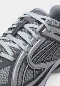 Κοντινό πλάνο γκρι αθλητικού παπουτσιού με επάνω μέρος από δίχτυ, ανοιχτό μπλε κορδόνια και μαύρο κλείστρο κορδονιών Skyfeet στη γλώσσα.