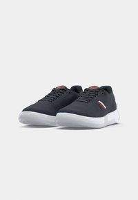 Mørkeblå sneakers med en tekstureret stofoverdel, hvid gummisål, rød og hvid stribet detalje på siden og matchende tungeetiket.