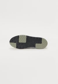 Sapatilha branca com sola de borracha preta e verde. Texturizada com pequenos padrões quadrados e grips circulares. Design leve e flexível.