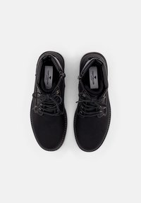 Botas de tobillo sintéticas negras con cordones y cremalleras laterales. Textura suave, puntera redonda y detalles de costura blanca. Logo visible en el interior.