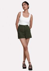 Hvid tanktop, olivengrøn høj talje shorts med frontlommer og knaplukning, sorte platform sandaler med krydsede stropper.