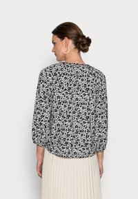 Blusa floral com cores azul-marinho e creme, corte descontraído, mangas três quartos e decote em forma de barco. Tecido texturizado com detalhes franzidos.