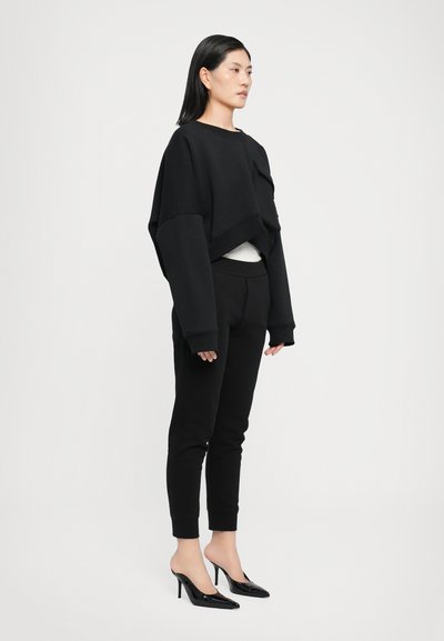 Black cropped sweatshirt with oversized sleeves, paired with black tapered pants and open-toe black heels, set against a white background.