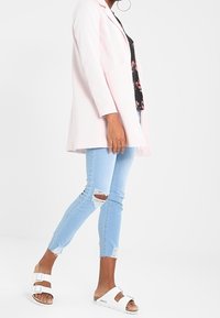 Light pink blazer with long sleeves, black floral top underneath, distressed light blue skinny jeans, and white slide sandals.
