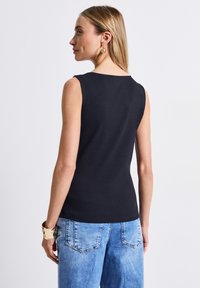 Top nero senza maniche con scollatura rotonda e silhouette aderente, abbinato a jeans in denim a gamba larga di colore blu chiaro con tasche posteriori.