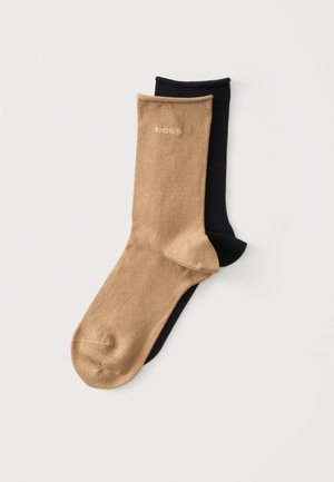 Zwei schlichte knielange Socken, eine beige mit kleinem hellem Logo nahe dem Bündchen und eine schwarze, flach auf einer weißen Oberfläche liegend.